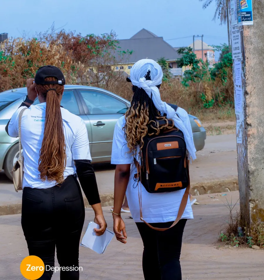 Two ZeroDepression volunteers in white t-shirts walking away from the camera, one with a backpack, carrying flyers on an outreach