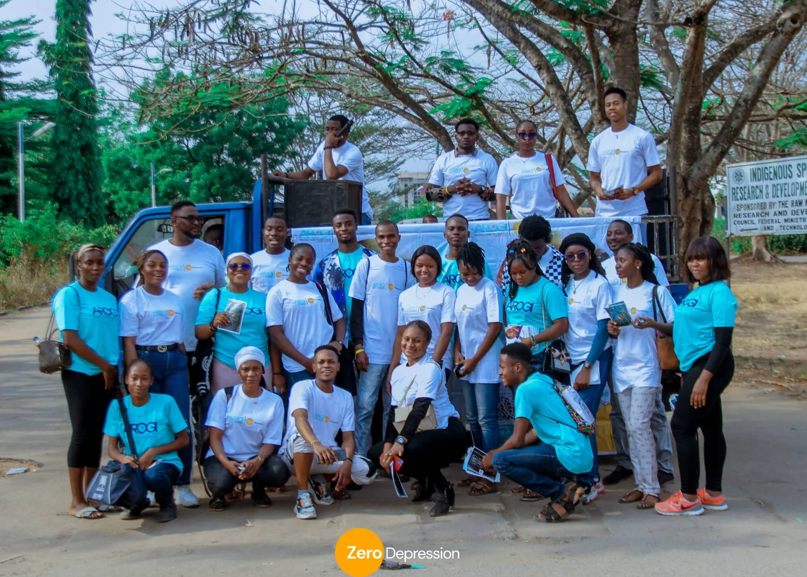 A large group of smiling ZeroDepression volunteers in white and blue t-shirts posing together outdoors in front of a truck